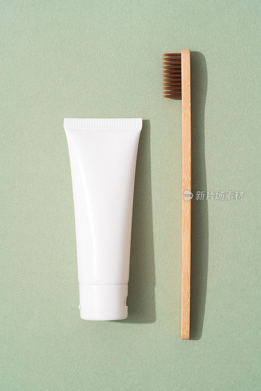 垂直图像木制竹牙刷和管有机矿物牙膏在绿色背景。白色塑料管牙膏。生态沐浴产品，模型