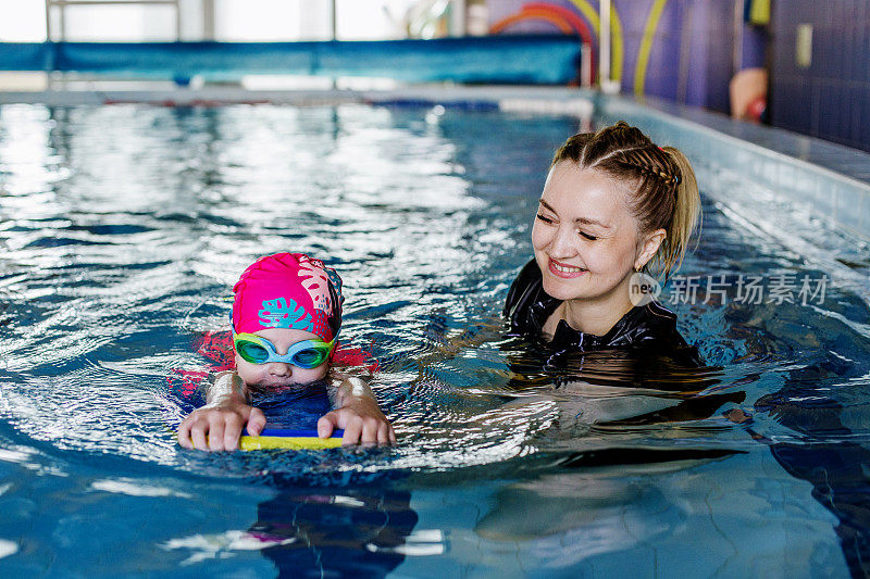 小孩在游泳池里学游泳。游泳教练教学龄前儿童在游泳池游泳