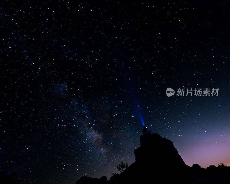 一个人坐在山顶上，在星夜里看星星的剪影