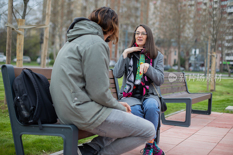 两个年轻的朋友坐在公园的长椅上用手语交谈