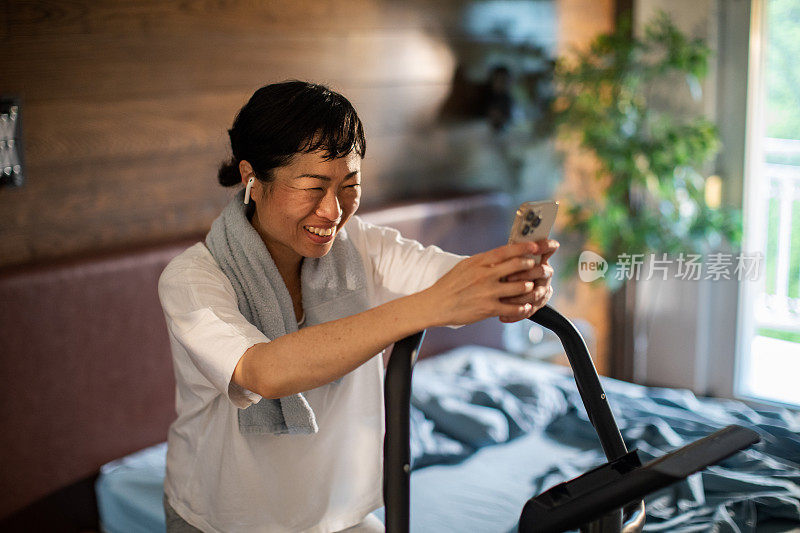 一名年轻的日本女子一边用智能手机一边在室内自行车上锻炼