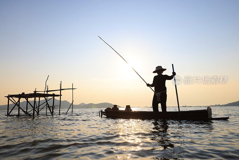 日出时渔夫撒网。亚洲渔民在木船上撒网捕淡水鱼，渔民在船上撒网。泰国