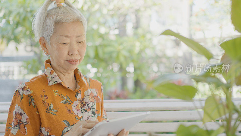 在户外使用数字平板电脑的亚洲老年妇女，银发上网者，积极拥抱科技的老年妇女