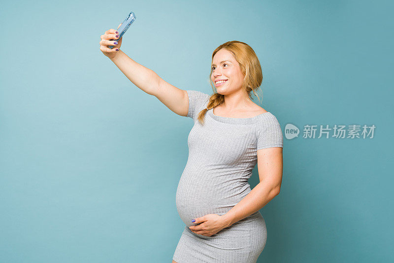 一位漂亮的孕妇在工作室用智能手机自拍，发布在社交媒体上