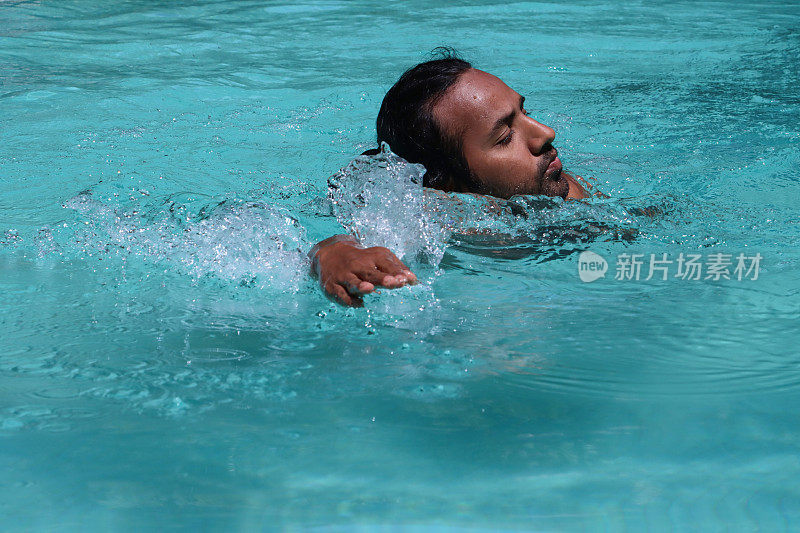 印度男子在晶莹剔透的水中做狗式划桨的特写，室外，游泳池，被波纹水扭曲的蓝绿色马赛克瓷砖，游泳和飞溅，波涛汹涌的水面反射，重点放在前景