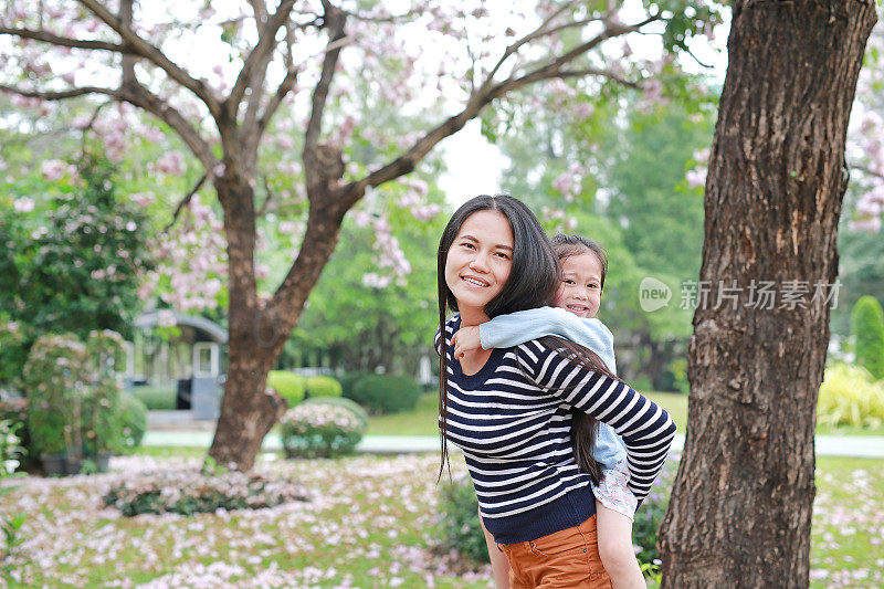 面带微笑的妈妈抱着她的小女孩在满是粉红色花朵的花园里。幸福美满的家庭。