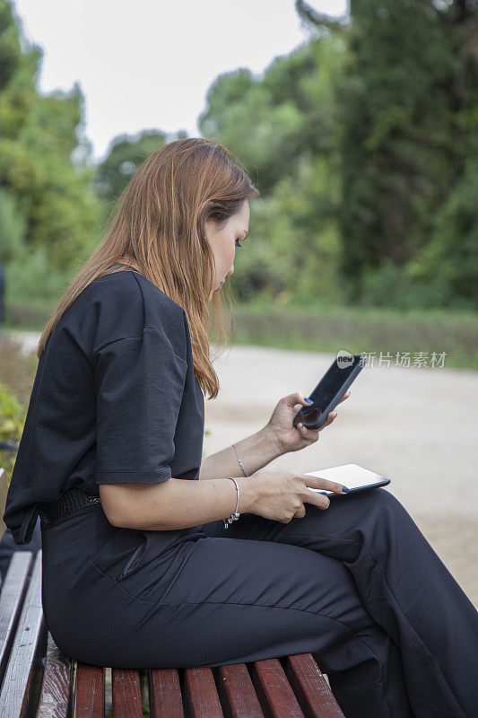 一个女人坐在公园的长椅上摆弄着她的平板电脑