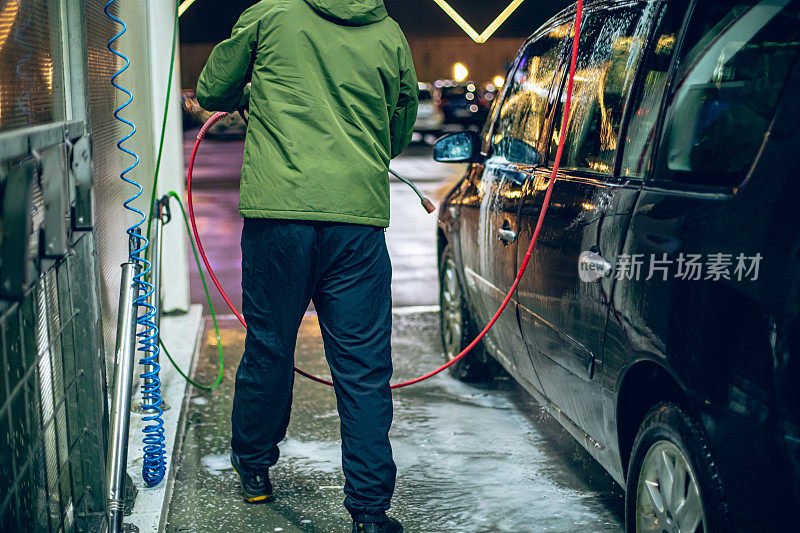 一名男子在自助洗车店用带加压水的软管洗车