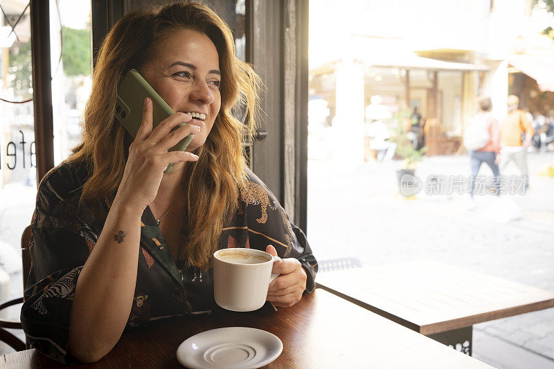 快乐的年轻女子在咖啡馆用手机喝咖啡