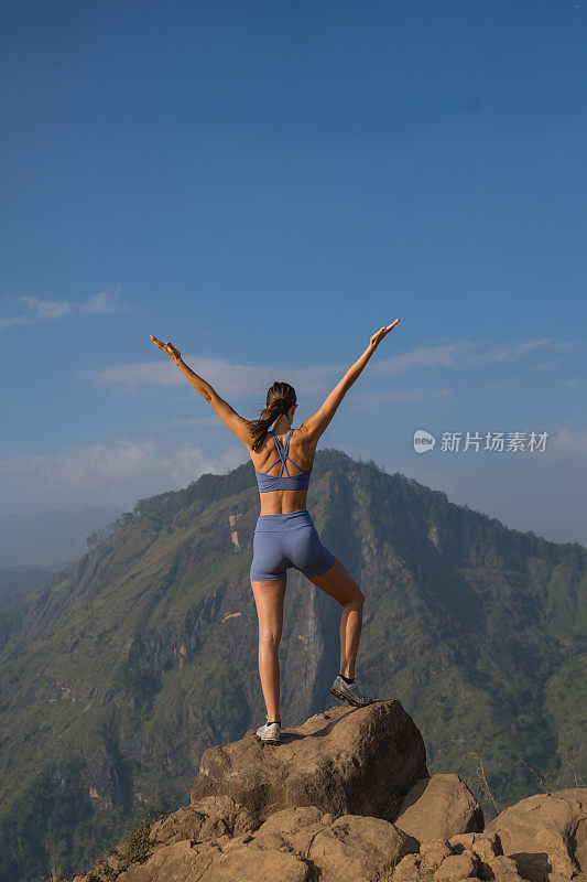 年轻女子站在山顶上伸开双臂