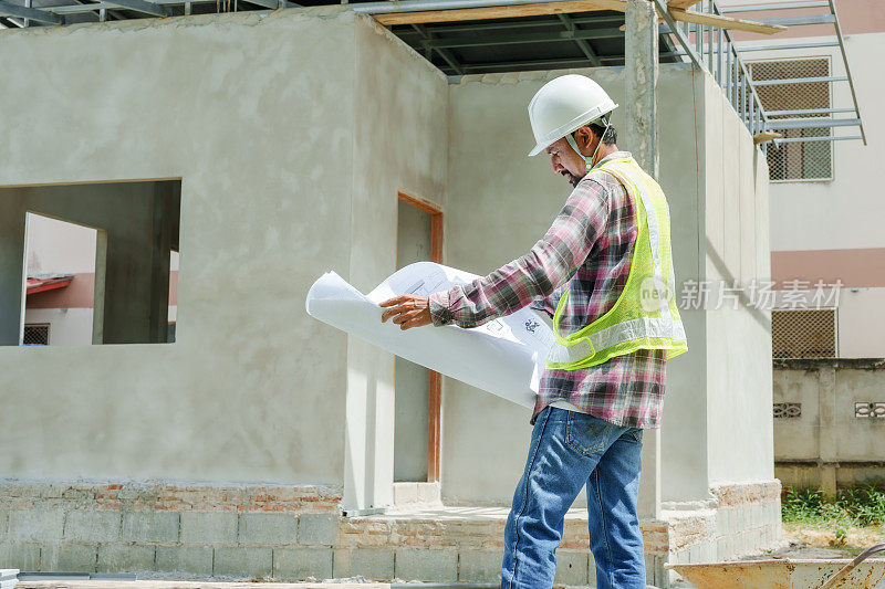 亚裔男子建筑监理工人工程师建筑雇员。戴上白色安全帽，看房子的结构图，背朝外面站着。