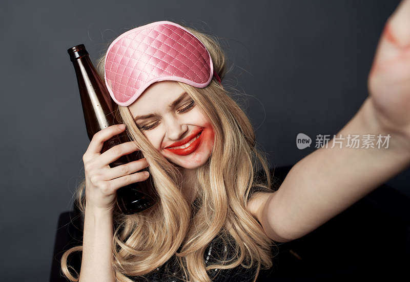一个喝醉酒的女人拿着一瓶啤酒在灰色的背景上玩得很开心，用她的手做着手势