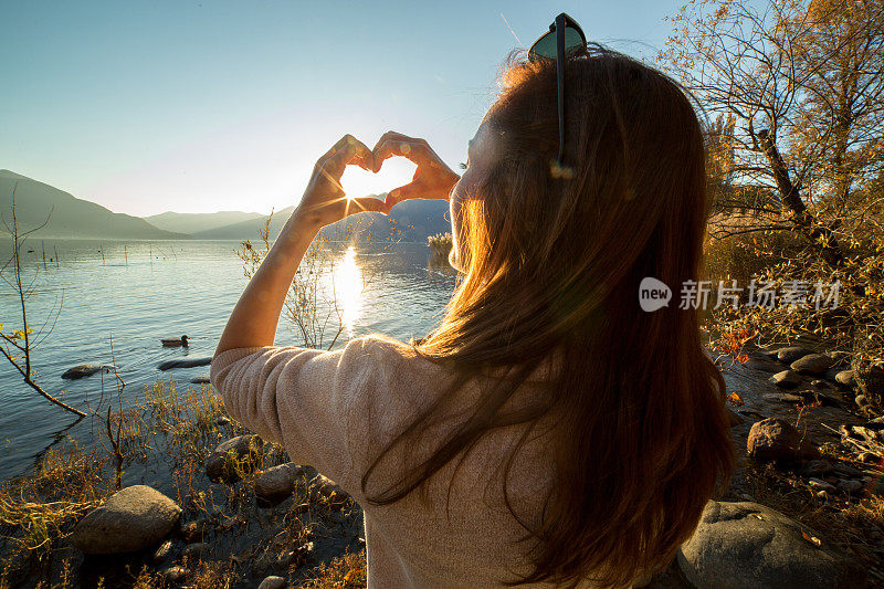 年轻女子在湖边做心形手指架