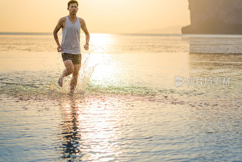 年轻的亚洲男子在海滩上奔跑，夕阳为背景