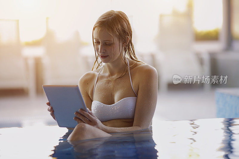 年轻女子放松在酒店游泳池使用数字平板电脑