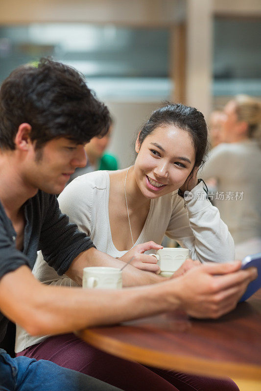 两个学生在咖啡店里拿着他们的平板电脑