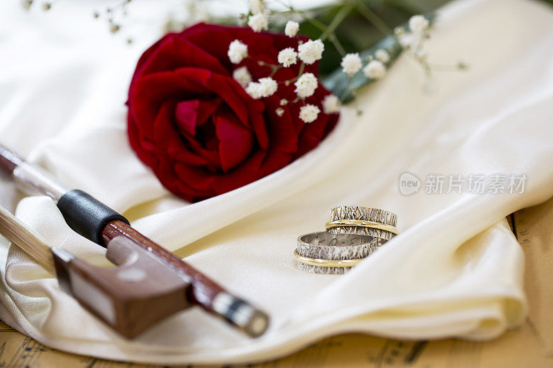 小提琴，红玫瑰，结婚戒指，酒和音乐音符在缎子织物上