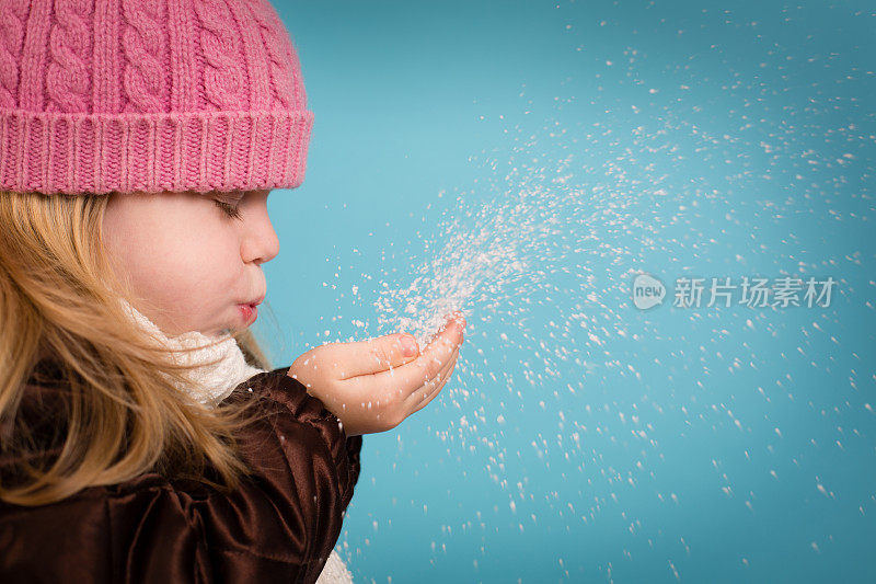 小女孩闭着眼睛，吹着一把雪