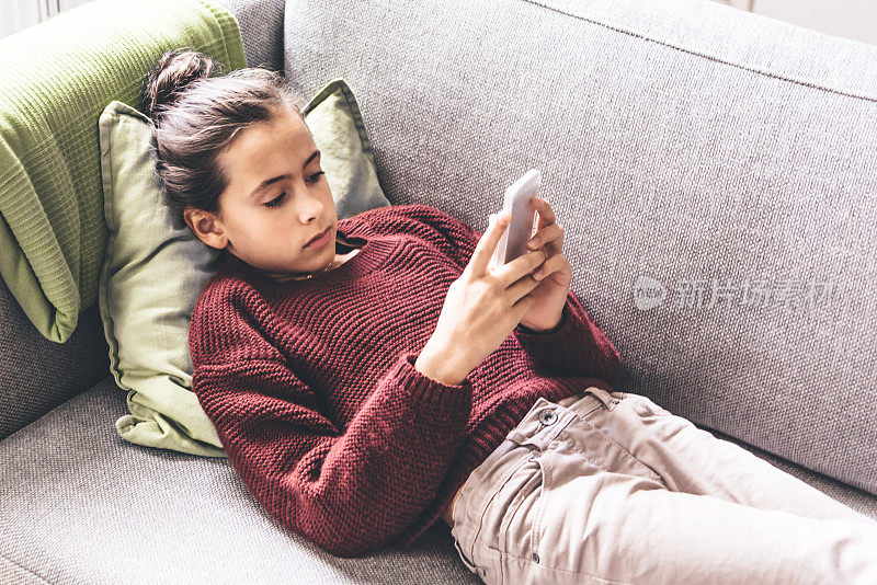 十几岁的女孩在沙发上放松，玩着智能手机