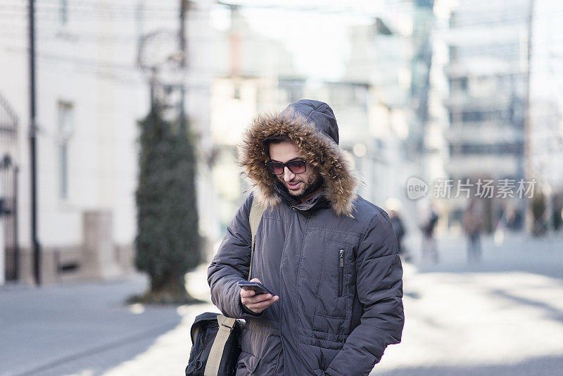 年轻男子穿着冬季夹克在户外用智能手机发短信