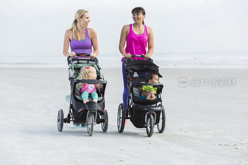 两个母亲和婴儿推着婴儿车在海滩上散步
