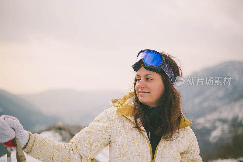 近景美丽的年轻女子在冬天的衣服站在一边，手拿木棍的背景雪山