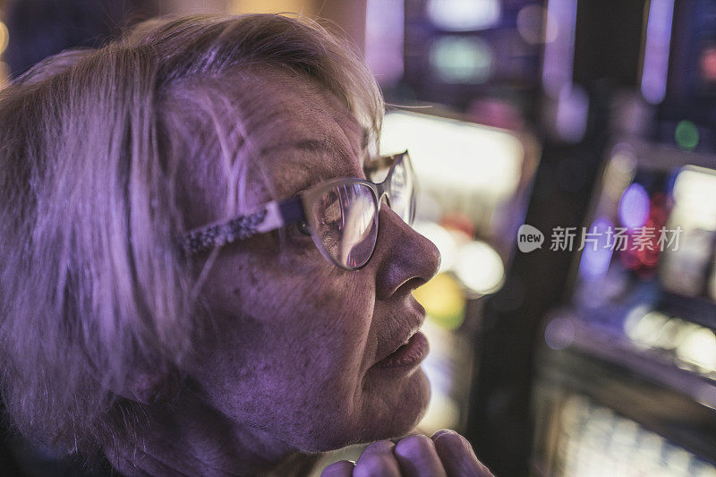 一位年长的女士，坐在老虎机前，正在拉斯维加斯赌场赌博，认真地查看屏幕。