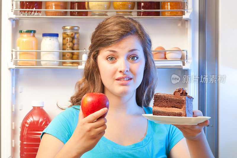 女人在打开的冰箱中选择健康或不健康的零食