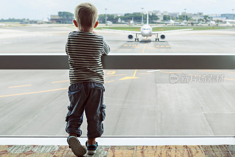 在机场大厅里，孩子透过窗户看飞机