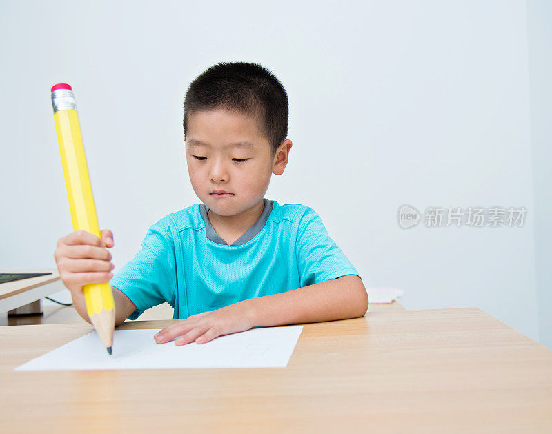 亚洲小男孩用一支大铅笔写字