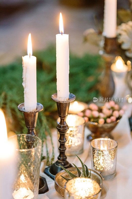 舒适、舒适、娱乐的概念。两根高高的白色蜡烛在烛台上燃烧着，周围是不同的小蜡烛，还有很棒的餐具