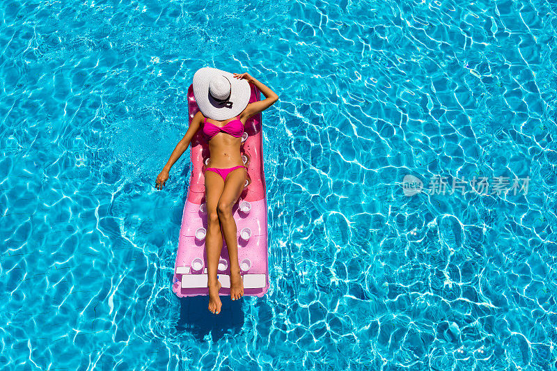 有魅力的女人正在游泳池里的一个漂浮的床垫上放松