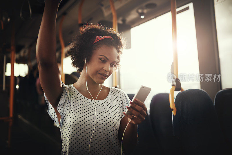 微笑的年轻非洲妇女在公共汽车上听音乐