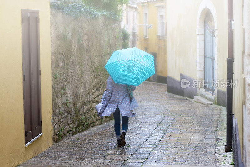 西西里岛:巴洛克小镇阴雨多雾多风的一天;拿着蓝伞的女人