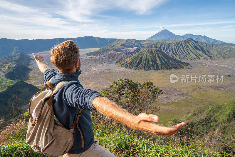 在印度尼西亚，年轻人徒步旅行，手臂伸开站在火山的山顶上，人们旅行的乐趣，冒险的概念，成功和成就