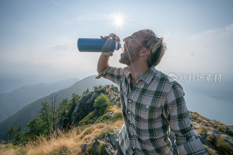 徒步男从水瓶中在山间小道上饮水