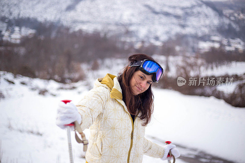 近景美丽的年轻女子在冬天的衣服站在一边，手拿木棍的背景雪山