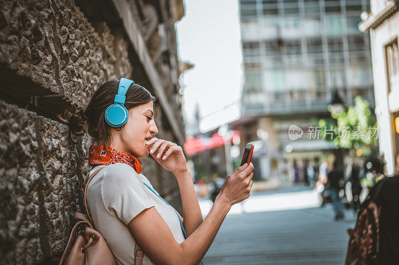 一名年轻女子正带着她的智能手机走在城市的路上