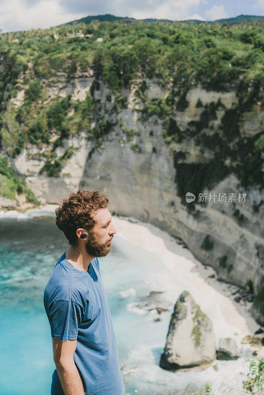 一个戴着无线耳机的男人从努萨佩尼达的悬崖上看海滩的风景