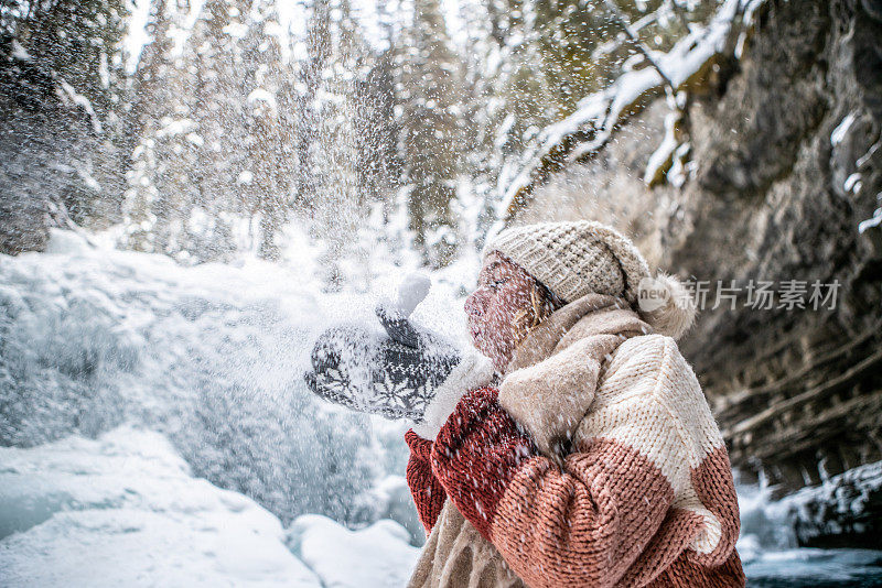 在冬天的仙境里，一个年轻的女人用温暖的手套吹着粉雪