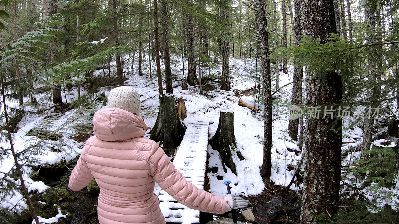 女性徒步旅行者走过被雪覆盖的木板路