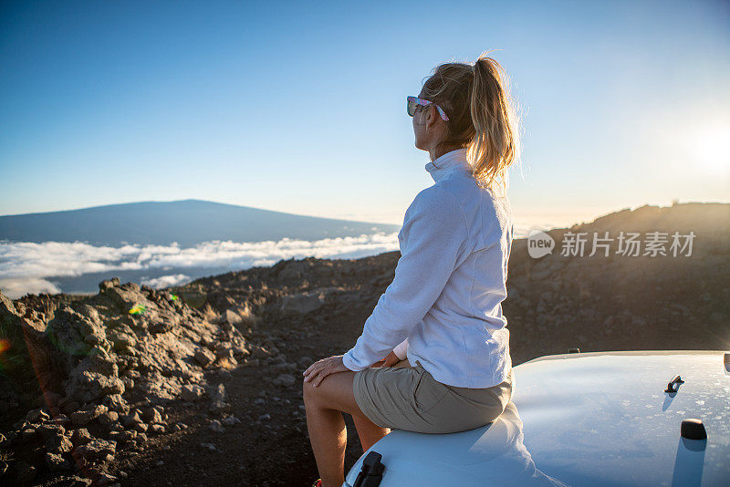 年轻女子坐在4x4引擎盖车看火山，在云端