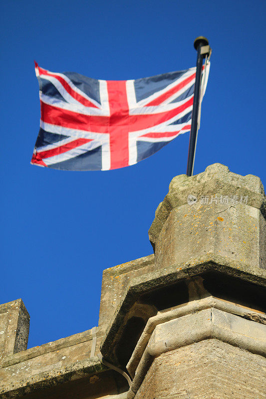 英国国旗在蓝天下从屋顶飘扬，红色，白色和蓝色的英国国旗，英格兰，苏格兰，威尔士和北爱尔兰，黑色旗杆上的国王的颜色英国国旗代表大不列颠