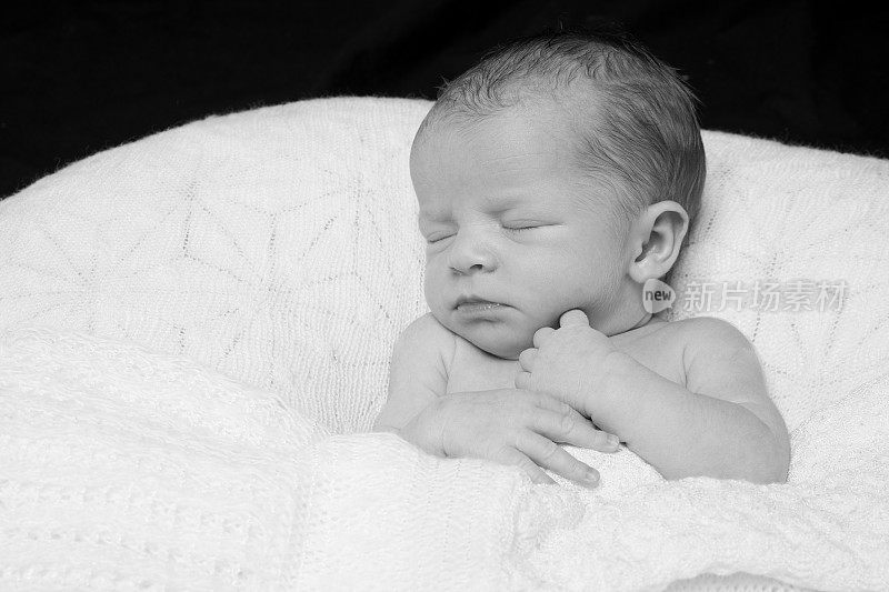 这是一张可爱的新生儿赤裸着身子躺在枕头上睡觉的亲密照片，上面盖着白色的毯子