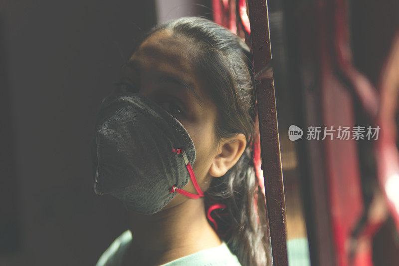 这个悲伤的女孩正在保护自己，戴着口罩，在家里自我隔离。