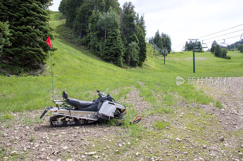 夏天，在绿山上的滑雪缆车旁边的草地和砾石上被困的雪地摩托