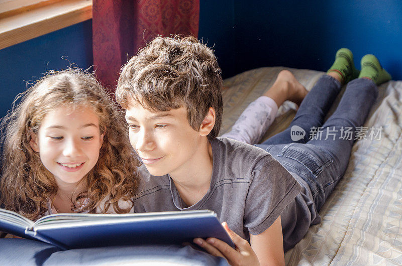 年轻的女孩和男孩在她的床上看书