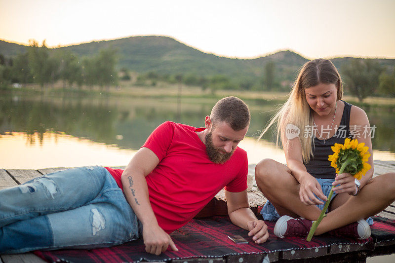 一对年轻夫妇坐在湖边的码头上欣赏日落