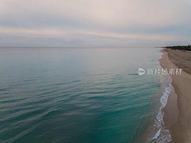 2021年1月18日，佛罗里达州棕榈滩海岸线上的蓝绿色海浪上的多云日出