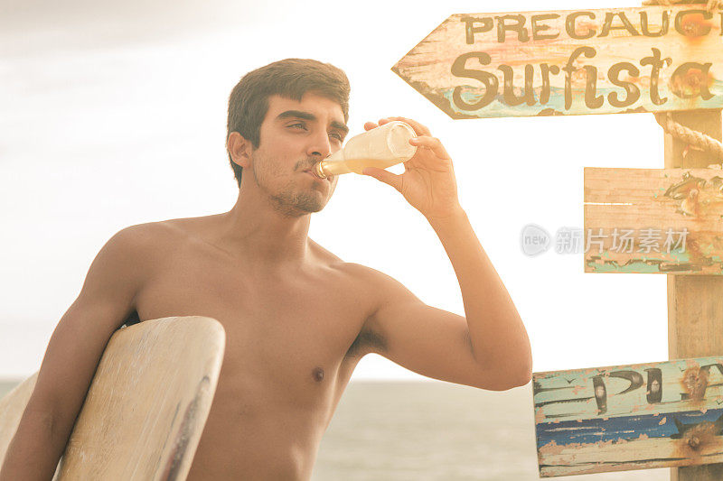 拉丁美洲厄瓜多尔瓜亚斯省的维拉米尔海滩，一名肌肉强健的拉丁冲浪者在海边喝着啤酒放松